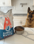 dog looking up onto counter with a bag of Simply Naked wild salmon dog food and a bowl of kibble